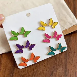 Detalle de un conjunto de pendientes de mariposa de esmalte sobre una tarjeta blanca