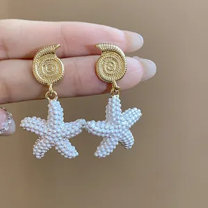 Primer plano de los pendientes de estrella de mar y concha bañados en oro de 18k