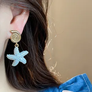 Vista macro detallada de pendientes de concha chapados en oro de 18k y estrella de mar azul