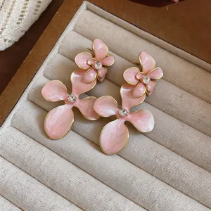Close-up of elegant pink enamel flower earrings with sparkling rhinestone centers.