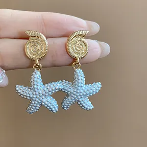 Primer plano de pendientes colgantes con concha bañada en oro 18k y estrella de mar azul