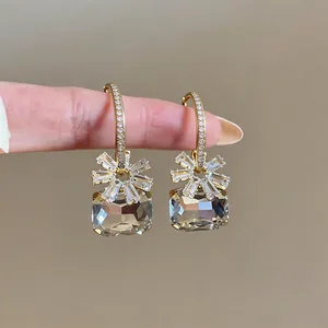Nahaufnahme von Gold-Ohrreifen mit Zirkon-Blume und rechteckigem Kristallanhänger
