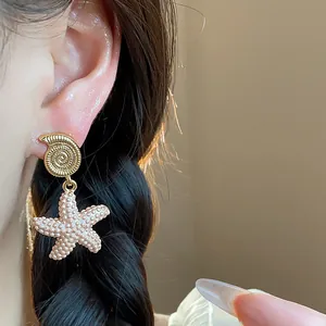 Primer plano de un pendiente de concha y estrella de mar dorada en una oreja