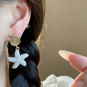 Primer plano de pendientes de concha y estrella de mar bañados en oro de 18 quilates