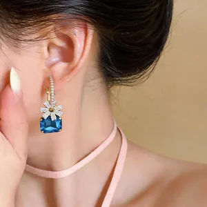 Nahaufnahme eleganter Blumen- und blauer Zirkonia-Goldcreolen am Ohr des Models