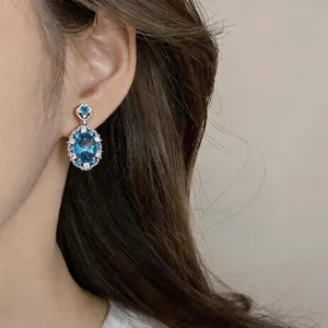 Close-up of sparkling oval blue zircon drop earrings worn on ear for elegant style
