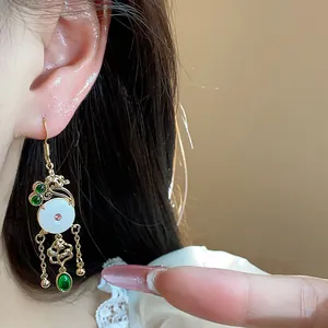 Detail of 14K gold plated earrings with green gems and white circular inlay