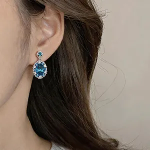Elegant macro view of sparkling blue oval zircon drop earrings worn on a model's ear.