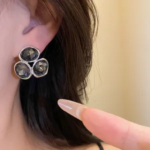 Close-up of a silver-tone cluster stud earring with dark grey faceted stones on an ear.