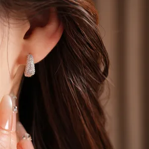 Close-up of elegant 14K white gold plated zircon pavé huggie earrings on ear