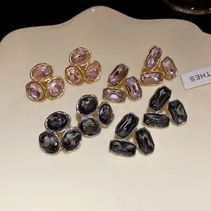 Close-up of various geometric rhinestone stud earrings in pink, lavender, and black tones