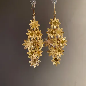 Vista dettagliata degli orecchini pendenti con fiori in metallo dorato e petali texturizzati.
