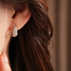 Macro view of a luxurious 14K gold plated zircon pavé stud earring worn on model's ear
