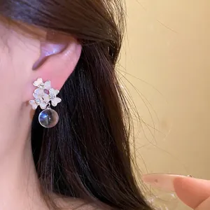 Boucles d'oreilles fleurs d'été avec goutte en cristal clair portées sur l'oreille.