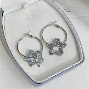 Vue détaillée de créoles argentées avec pendentifs étoiles en résine bleue en boîte.