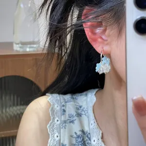 Nahaufnahme von eleganten Creolen mit zarten blau-weißen Verlaufsblumen an einem Model