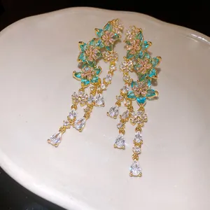 Close-up detail of elegant gold-toned earrings with turquoise zircon flower and waterdrop tassels.