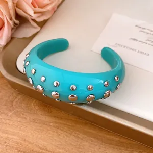 Turquoise resin open cuff bracelet with silver-tone metal dome studs on a gold display tray