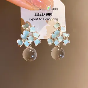 Détail de boucles d'oreilles fleurs en émail bleu avec perles claires sur carte.