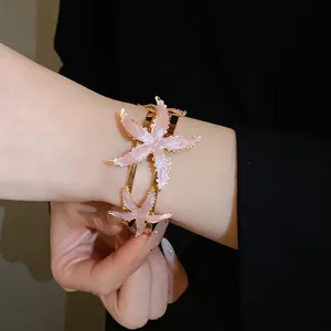 Elegant gold-plated open cuff bracelet featuring two sparkling pink starfish enamel motifs