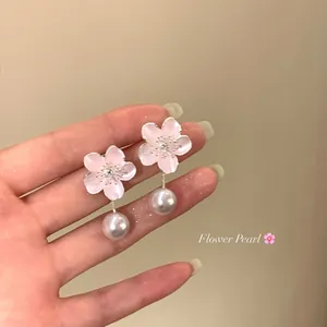 Detailed close-up of elegant pink cherry blossom earrings with pearl drops held in hand