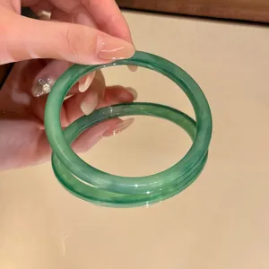 Elegante bracciale rigido verde traslucido mostrato su una superficie a specchio.