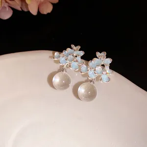 Détail de boucles d'oreilles fleurs en émail bleu clair avec gouttes en boule de verre