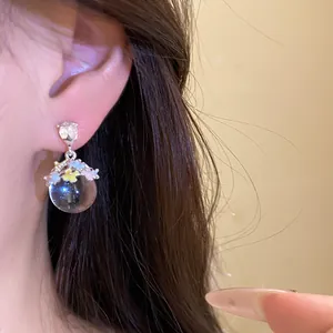 Gros plan détaillé d'une boucle d'oreille sphérique avec fleurs en émail colorées et cristal.