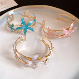 Detailed view of three gold-plated starfish open bangles with blue pink and white enamel