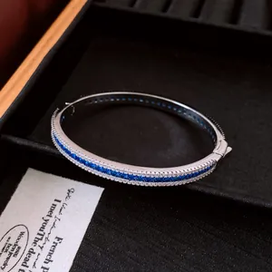 Detail view of a retro palace style silver bangle with blue and white cubic zirconia