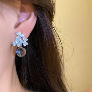 Détail de boucles d'oreilles fleur bleue avec un pendentif orbe en verre clair