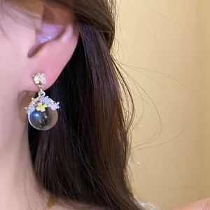 Gros plan sur des boucles d'oreilles fleurs en émail avec une sphère transparente.