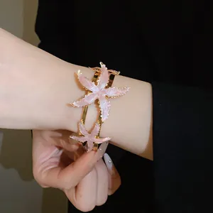 Close-up of a gold metal cuff bracelet featuring glittery pink starfish charms.