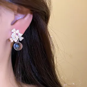 Gros plan de boucles d'oreilles fleurs émaillées avec perle transparente, style forêt.