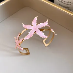 Close-up of gold-plated cuff bracelet featuring pink enamel starfish charms.
