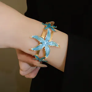 Detailed view of a gold-finish cuff bracelet with vibrant blue enamel starfish motifs.