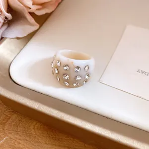 Detailed close-up of a cream resin ring with sparkling clear stone inlays on a gold tray