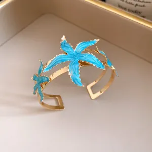 Close-up detail of a vintage-style gold open cuff bracelet featuring blue enamel starfish.