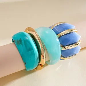 Detailed macro view of stacked colorful acrylic and gold-toned geometric chunky bracelets