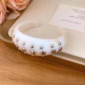 Detailed view of a white resin cuff bracelet adorned with silver round rivets