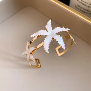 Close-up of white enamel starfish ornaments on a gold-plated open cuff bangle