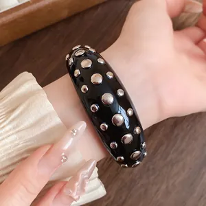 Close-up of a chunky black resin bangle with silver metal rivet studs on a wrist.