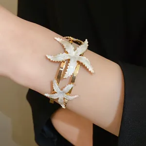 Close-up view of a gold-toned starfish open bangle featuring elegant white enamel texture