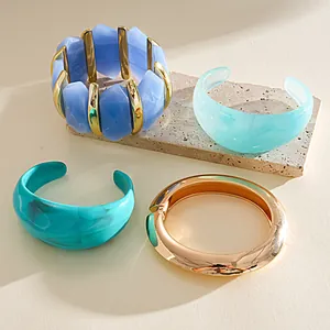 Group of colorful acrylic geometric bangles and chunky gold tone bracelet on stone slab