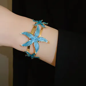Close-up of a gold metal starfish open cuff bracelet with vibrant blue enamel details.