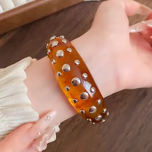 Close-up detail shot of an amber resin bracelet featuring embedded silver-tone metal studs
