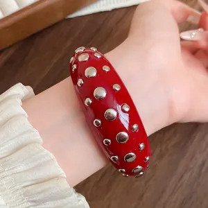 Macro detail of a red resin cuff bracelet featuring polished silver-tone metal studs.