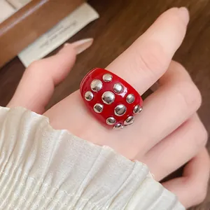 Close-up detail of a vibrant red resin ring with silver round metal studs worn on a finger