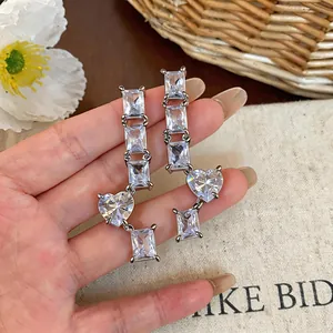 Detailed view of silver needle earrings featuring square and heart-shaped zircon stones