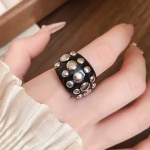Detailed close-up view of a stylish black resin ring with metallic silver rivets on a finger.